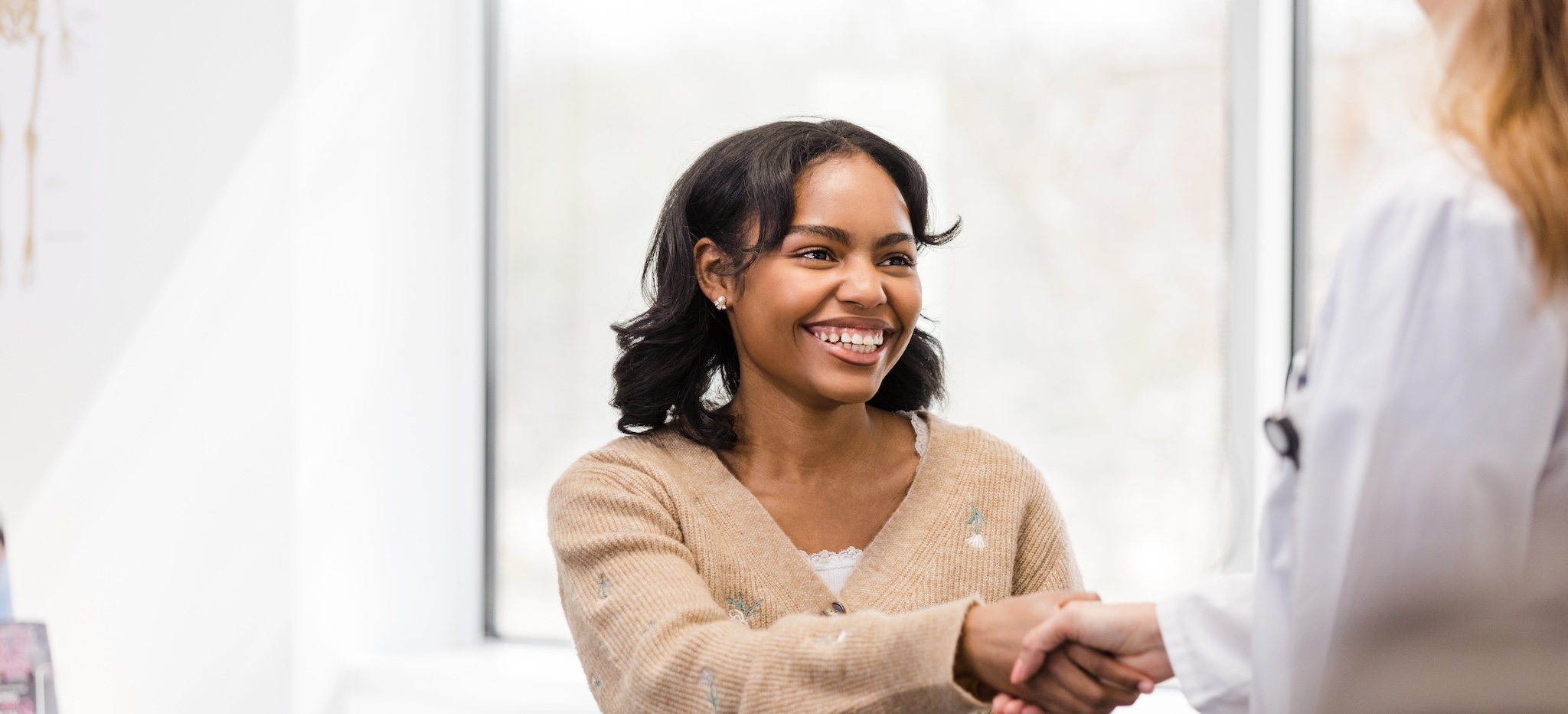 The teenage girl greets the unrecognizable female doctor with a big, toothy smile and a handshake.